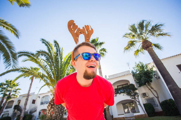 Urlaub und Menschen-Konzept - lustiger Mann mit weihnachtlichen Hirschhörnern, der draußen lächelt - Foto, Bild