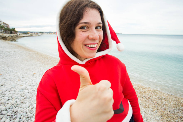 Menschen, Feiertage und Weihnachten - fröhliche Frau mit Weihnachtsmütze macht Selfie und zeigt Daumen hoch - Foto, Bild