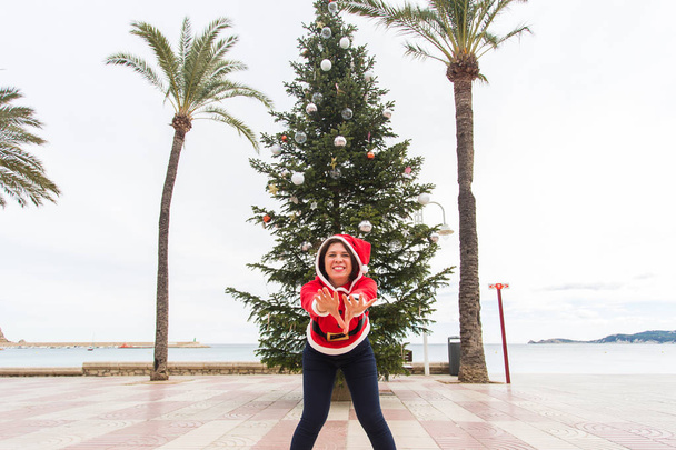 Noël, vacances et concept d'humour - jeune femme heureuse s'amuser en costume de Noël à l'été près des paumes et de l'arbre de Noël
 - Photo, image