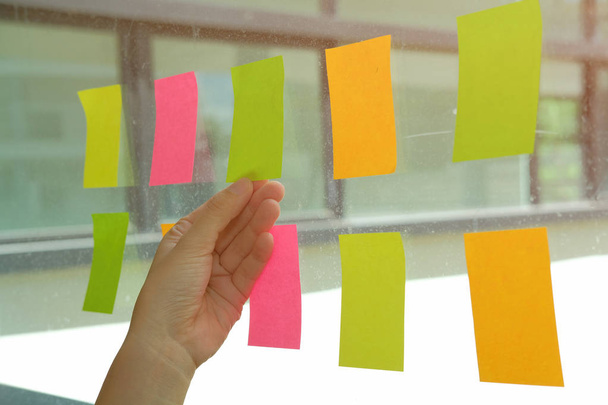 kézzel tart öntapadó jegyzetek a munkahelyen üvegfal. Öntapadó jegyzet könyv emlékeztető ütemezés a kreatív ötlet & üzleti ötletgyűjtéshez használható - Fotó, kép