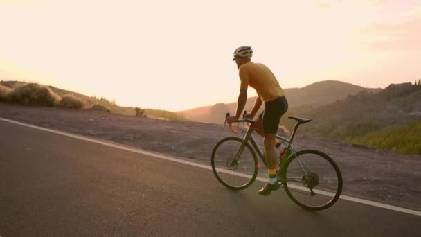 Um ciclista profissional em um capacete e equipamentos esportivos cavalga em uma estrada de montanha ao pôr do sol em câmera lenta. Steadicam
 - Filmagem, Vídeo