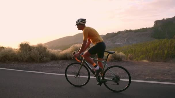 Egy profi kerékpáros sisak és sport felszerelések, lovagolni egy hegyi autópálya napnyugtakor a lassú mozgás. Steadicamnél - Felvétel, videó