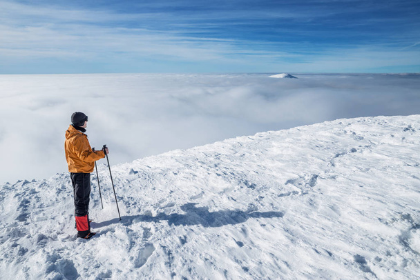 Winter hiking. Tourist on snowy mountain top enjoying beautiful view of cloudscape. - Фото, зображення
