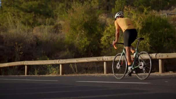 Profesionální cyklista v helmě a sportovní vybavení jezdí na horské silnici - Záběry, video