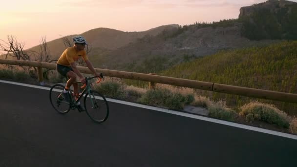 Een wielrenner in een helm en sport apparatuur rijdt op een berg serpentine bij zonsondergang in de richting van de vulkaan. Steadicam - Video
