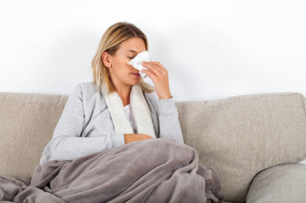 Picture of a sick young lady sitting on the couch and blowing her runny nose - Fotoğraf, Görsel
