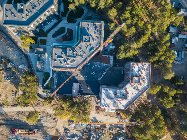 Aerial view of the construction of three elite residential buildings on the river bank in the middle of a green coniferous forest with a favorable environment, a lot of equipment costs near the site - Foto, afbeelding