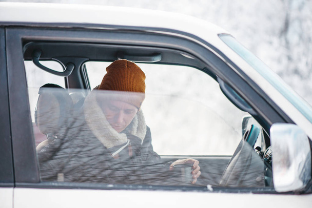 Matkustaja nuori mies istuu kupin kuumaa juomaa autossa talvella
. - Valokuva, kuva