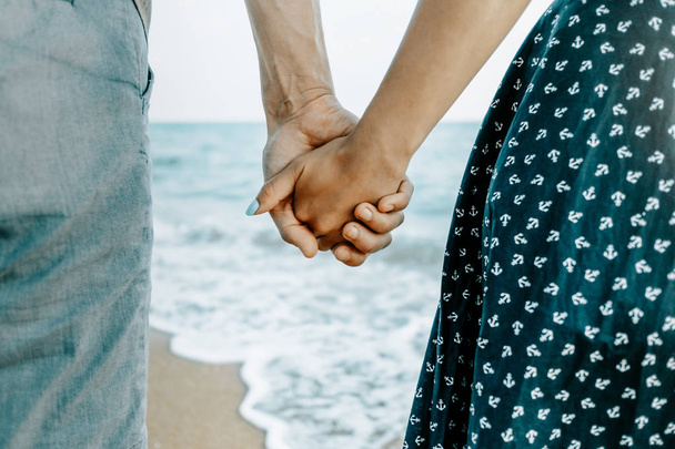 Unrecognizable couple in love holding hands together on sea coast, rear view, close-up. - Zdjęcie, obraz