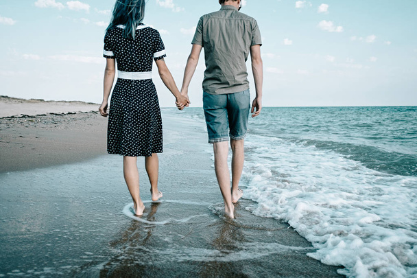 Νέοι αγαπώντας ζευγάρι περπάτημα στο άμμο ακτή κοντά στη θάλασσα και κρατώντας τα χέρια μαζί, παραλία καλοκαιρινές διακοπές. - Φωτογραφία, εικόνα