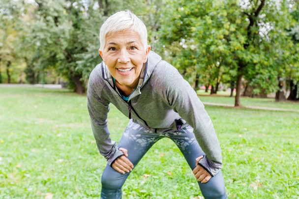 Зрелая женщина в спортивной форме делает упражнения по фитнесу в природе, тренировки на открытом воздухе
. - Фото, изображение