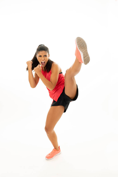 Young and furious latin woman in fight and kick boxing training workout throwing aggressive kick attack isolated on white background in fitness sport gym exercise and personal defense concept. - Φωτογραφία, εικόνα