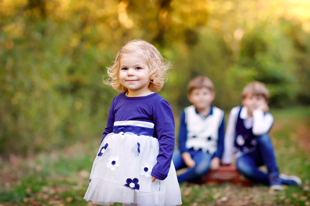 Üç kardeş çocuğunun portresi. Küçük tatlı kız kardeş ve iki erkek kardeş arka planda sonbahar ormanında birlikte eğleniyorlar. Mutlu sağlıklı aile oyunları, yürüyüş, aktif - Fotoğraf, Görsel
