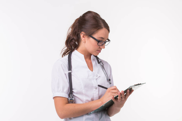 Medizinerin hält Stift in der Hand und schreibt etwas auf Klemmbrett auf weißem Hintergrund. - Foto, Bild