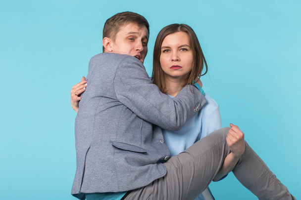 Family problems, responsibility, feminism and relationship concept - Woman carrying man in her arms on blue background - Photo, Image