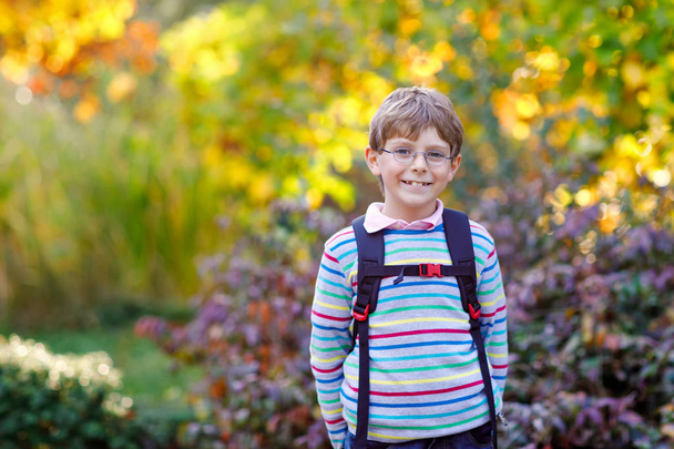 Joyeux petit garçon avec des lunettes et un sac à dos ou une sacoche lors de son premier jour à l'école le jour ensoleillé d'automne. Enfant en plein air avec des érables jaunes et lisez sur le fond, concept de retour à l'école
 - Photo, image