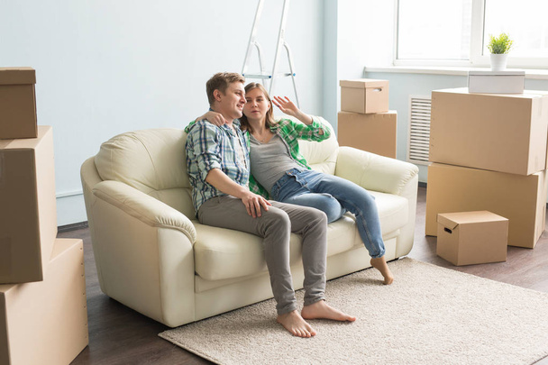Меблі, переїзд і концепція людей - щаслива пара сидить на новому дивані в порожній квартирі серед ящиків і сперечається про щось
 - Фото, зображення
