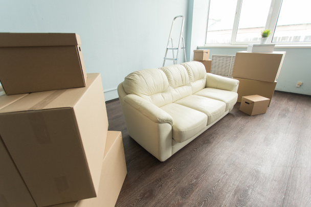 Relocation, moving and real estate concept- a new white sofa in empty room between an amount of boxes - Photo, Image