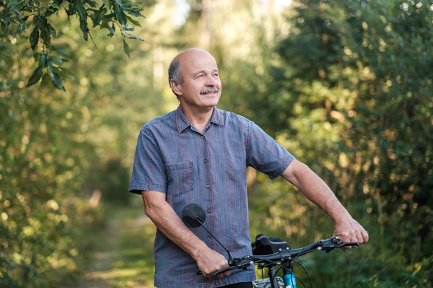fröhlicher älterer Mann, der an einem schönen sonnigen Tag in einem Park Fahrrad fährt. aktives Leben im Alter. Konzept des Sports im Urlaub - Foto, Bild
