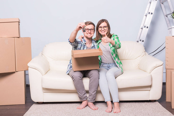 Mudanza, reubicación y nuevo concepto de hogar - pareja joven divirtiéndose en el sofá rodeado de cajas
 - Foto, Imagen