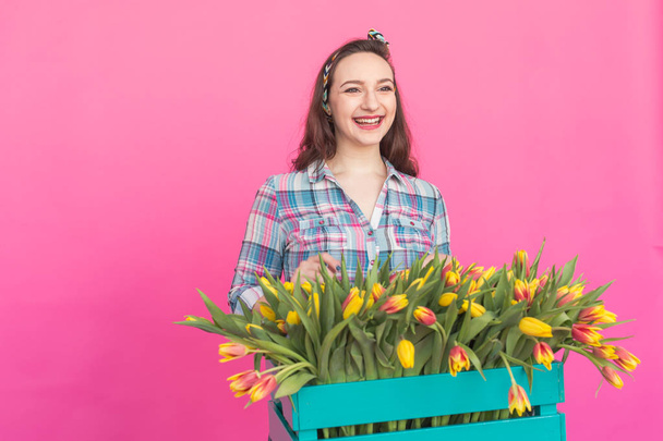Morena mujer joven con montón de tulipanes sobre fondo rosa
 - Foto, imagen