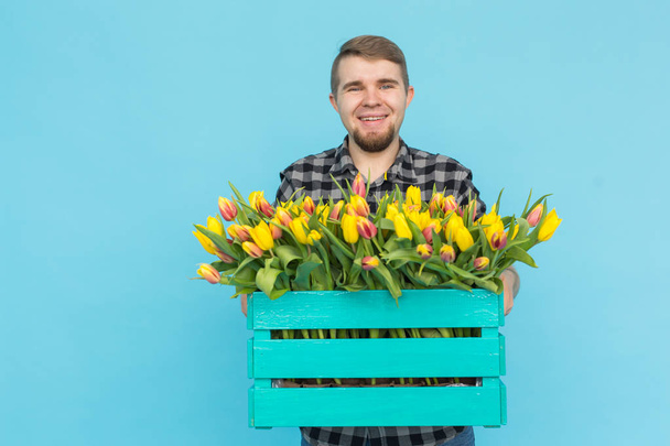 Valkoihoinen mies puutarhuri laatikko tulppaanit nauraa sinisellä taustalla
 - Valokuva, kuva