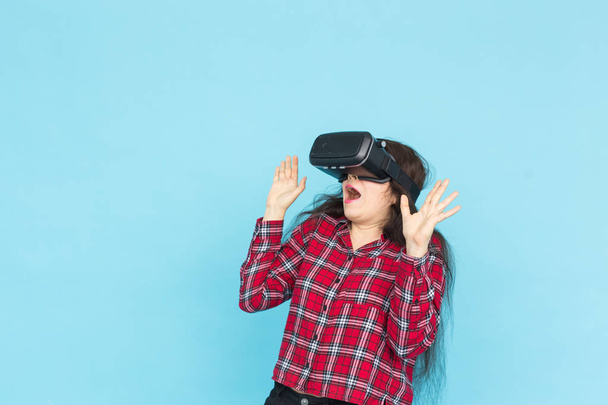 Technologie en mensen concept - jonge vrouw testen vr-bril met handen omhoog op blauwe achtergrond. - Foto, afbeelding