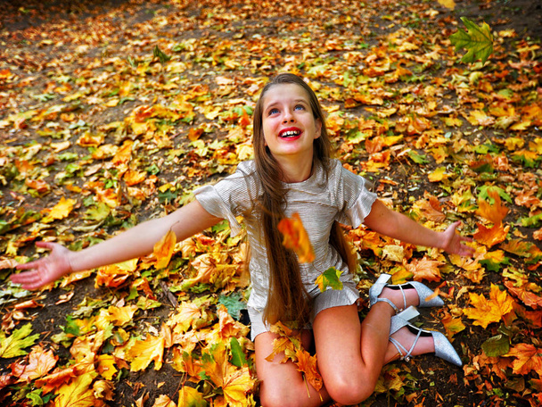 Φθινοπωρινή μόδα φόρεμα κορίτσι παιδί κάθεται πτώση φύλλα πάρκο εξωτερική. - Φωτογραφία, εικόνα