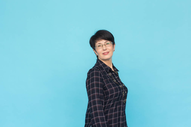 Portrait of middle-aged woman with short hair wearing glasses standing against blue background with copy space - 写真・画像
