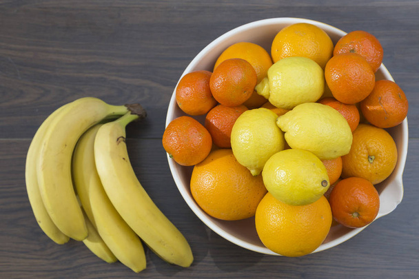 overhead view of a fruit bowl with citrus fruits, oranges, tangerines and lemons, next to a cluster of bananas - Photo, Image
