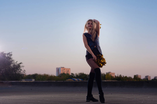 Girl cheerleader with pompoms dancing outdoors on the roof at sunset - Foto, Imagem