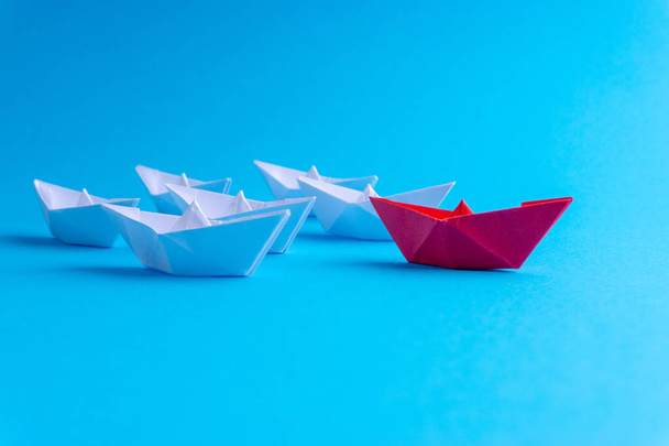 White and red paper boat or ship in one direction on blue background. Business for innovative solution concept with selective focus - Photo, Image
