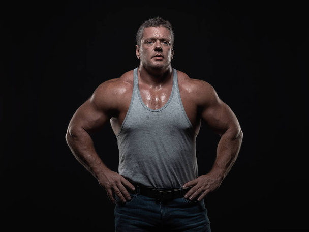 Powerful muscular bodybuilder posing on a black background. The concept of strength and health - Фото, зображення