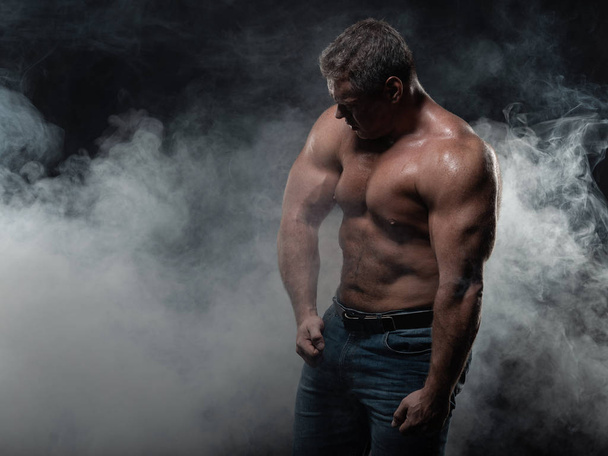 Powerful muscular bodybuilder posing on a black background. The concept of strength and health - Foto, Imagen