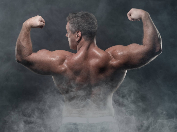 A powerful muscular man shows biceps on a black background. Strength and fitness concept - Фото, зображення