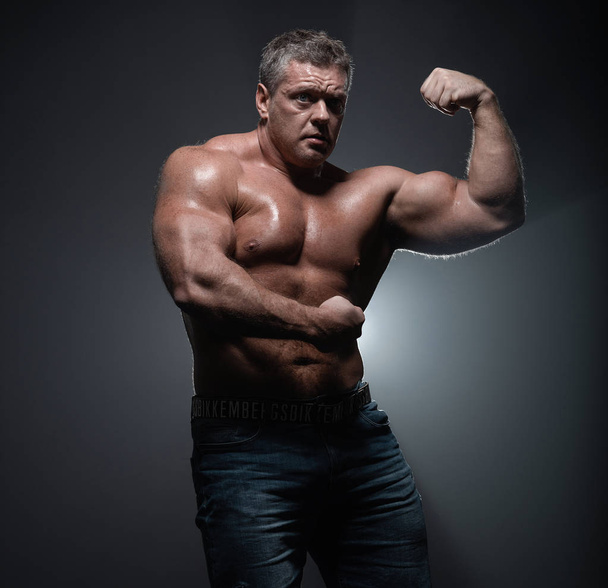 Powerful muscular bodybuilder posing on a black background. The concept of strength and health - Foto, immagini