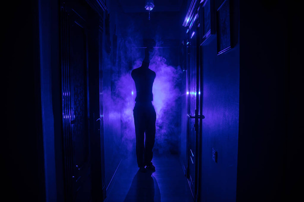 暗い廃屋で不気味なシルエット。ホラー ハロウィンのコンセプトです。センターに立っているホラー人のシルエットと暗い廊下。トーンの光と背景の霧. - 写真・画像