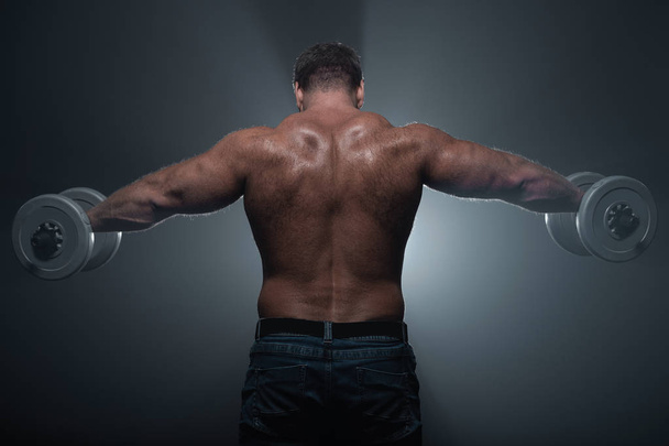 Powerful muscular man trains with dumbbells on black background in smoke - Zdjęcie, obraz
