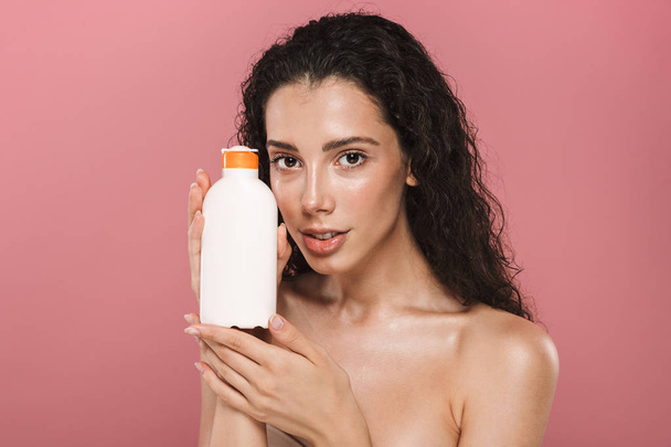 Portrait of pretty beautiful young woman posing isolated over pink background take care of her skin holding cream lotion gel. - Φωτογραφία, εικόνα