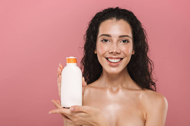 Portrait of happy smiling beautiful young woman posing isolated over pink background take care of her skin holding cream lotion gel. - Фото, зображення