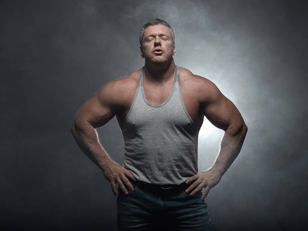 Powerful muscular bodybuilder posing on a black background. The concept of strength and health in smoke - Fotografie, Obrázek