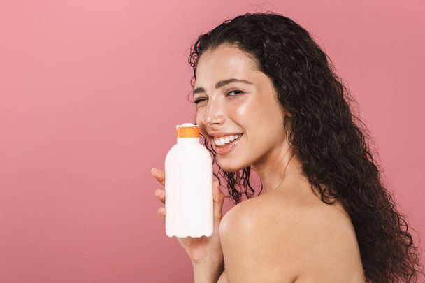 Portrait of happy smiling beautiful young woman posing isolated over pink background take care of her skin holding cream lotion gel. - Foto, Imagem