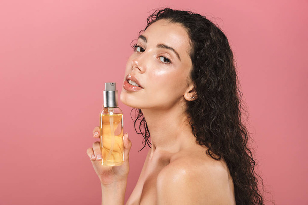 Portrait of pretty beautiful young woman posing isolated over pink background take care of her skin holding oil. - Foto, imagen