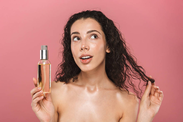 Portrait of pretty beautiful young woman posing isolated over pink background take care of her hair holding oil. - Photo, Image