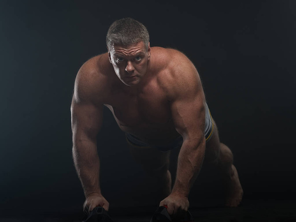 Powerful muscular man does pushups in the smoke on a black background - Fotografie, Obrázek