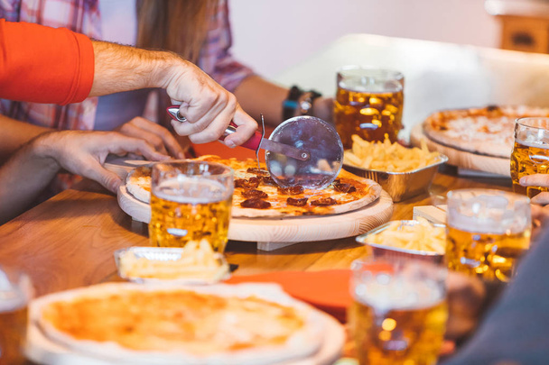 Group of college students cutting home made or take away pizza. Best friends dinning with pizza and beer. Close-up image with focus on cutter. - Zdjęcie, obraz