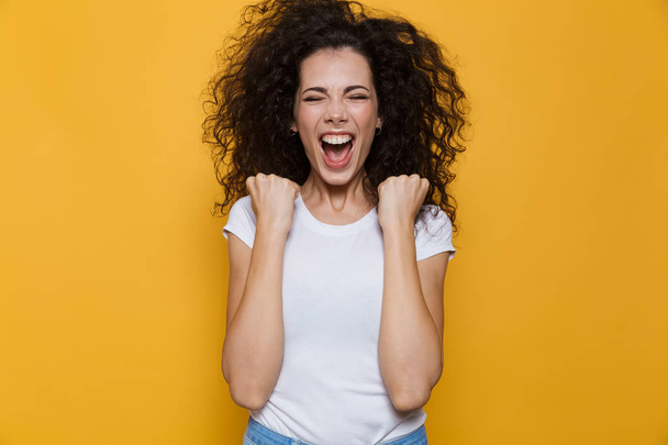 Image of emotional woman 20s with curly hair shouting and clenching fists isolated over yellow background - Fotoğraf, Görsel
