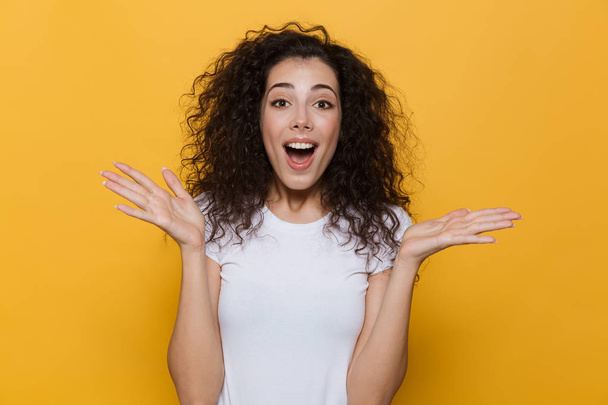 Image of gorgeous woman 20s with curly hair laughing and throwing up hands isolated over yellow background - Foto, imagen