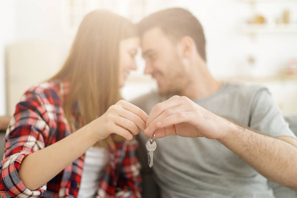 Young happy smiling couple holding set of keys, sitting on sofa face to face. New family concept - Photo, Image