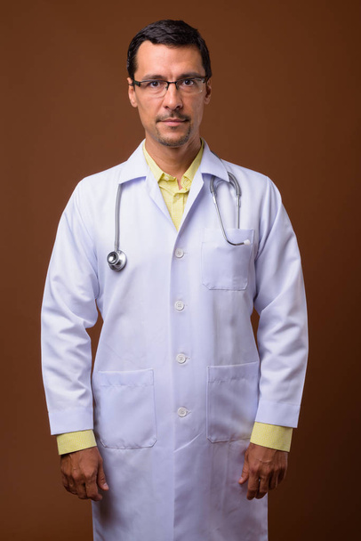 Portrait of handsome man doctor against brown background - Fotoğraf, Görsel
